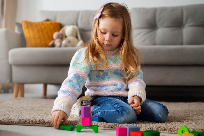 Young girl playing with colorful blocks on the floor, capturing moments of innocent family drama and bonding.