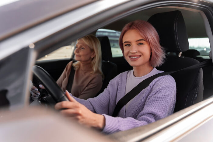 Young woman with braces driving a car with an older woman as passenger, showing small tricks that make being a grown-up easier.
