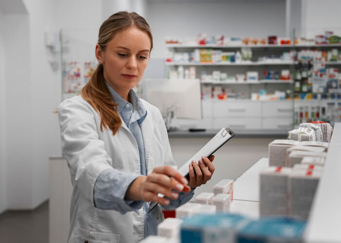 Pharmacy employee in white coat inspecting medication boxes, revealing dark truths about the pharmaceutical industry.