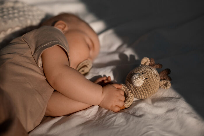 Sleeping baby holding a knitted toy, evoking unresolved mysteries people carry with them in quiet moments.