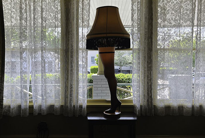 Unique white elephant gift lamp shaped like a woman's leg in fishnet stocking standing by a lace-curtained window.