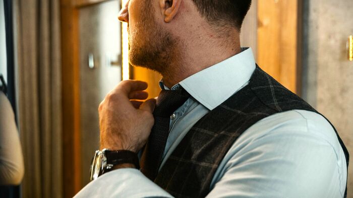 Man in a dress shirt and vest adjusting his tie, contemplating ambiguous situations to decide who is at fault or right.