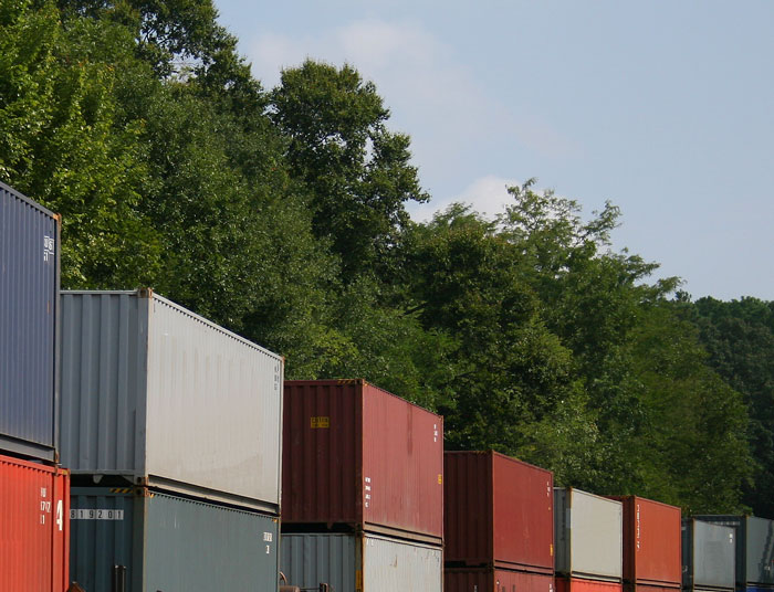 Stacked colorful shipping containers near dense green woods with clear sky, highlighting people who couldn't sleep after spending time in the woods