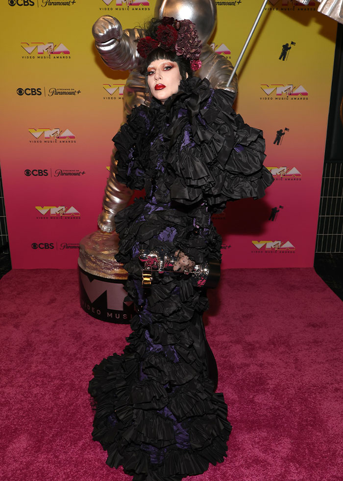 Person wearing an elaborate black ruffled outfit with red floral headpiece at an event showcasing celebrity fashion disasters 2025.