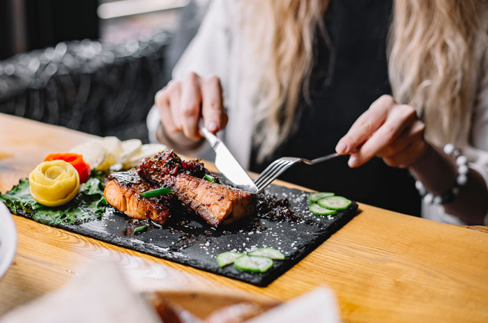 Person cutting grilled salmon on a plate at dinner while brother makes bil pay dinner in a restaurant setting