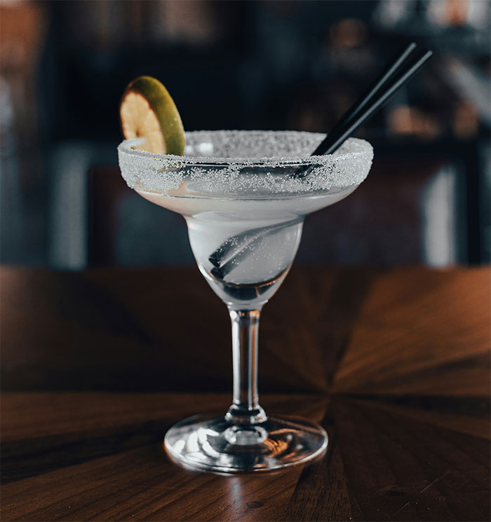 Margarita cocktail with salted rim and lime slice on wooden table, waiter serves first date disaster setting. Margarita cocktail with salted rim and lime slice on wooden table, waiter serves first date disaster setting.