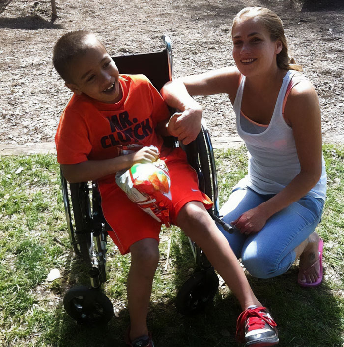 Woman kneeling beside smiling boy in wheelchair outdoors, representing Cinnabon worker&rsquo;s daughter reacting to racist tirade.