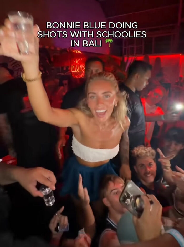 Bonnie Blue raising a shot glass in a crowded Bali club, surrounded by people enjoying a night out and taking photos.