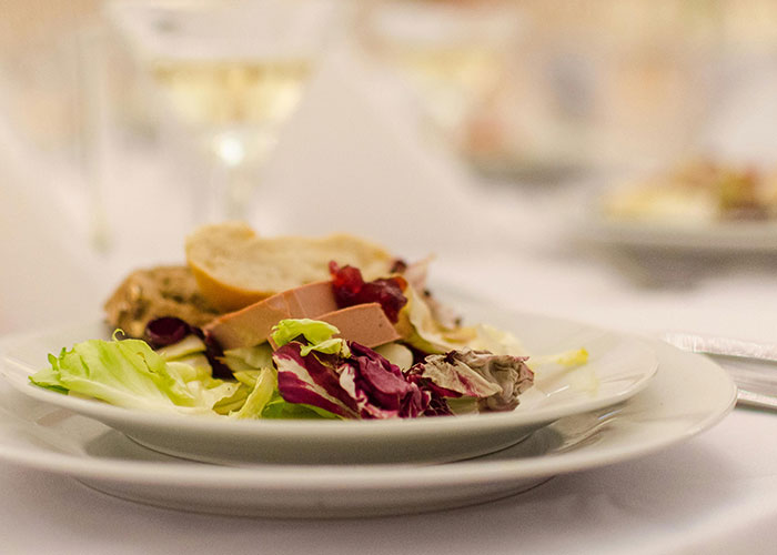 Salad and bread served on a white plate in a luxury dining setting, highlighting rip-offs in luxury industries.