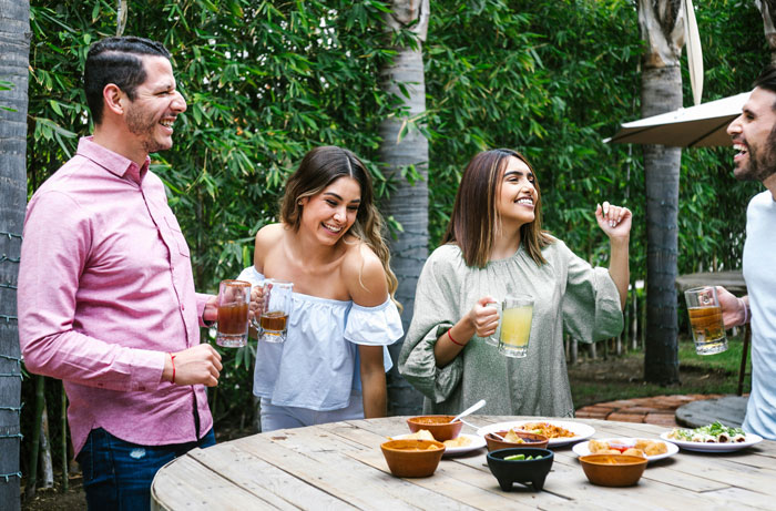 Four friends enjoying drinks and food outdoors, with the brother making his bill pay dinner in a relaxed setting.