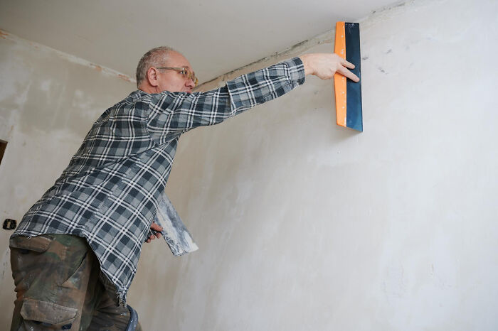 Man smoothing plaster on wall indoors, illustrating bizarre things people ever seen through a neighbor's window.
