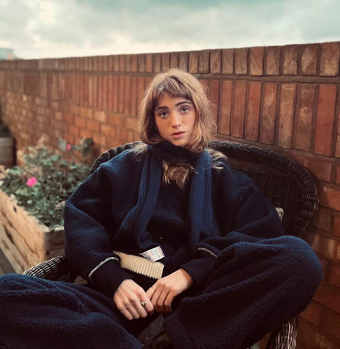 Stranger Things star Natalia Dyer sitting outdoors in dark cozy clothes, with a thoughtful expression and soft natural light.