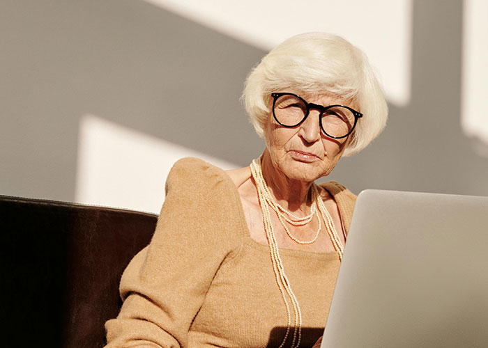 Elderly woman with glasses looking at laptop with a shocked expression, illustrating unhinged things their MIL said online.