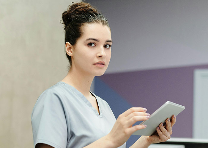 Young female healthcare worker in scrubs using tablet, illustrating unprofessional things doctors have said to patients.