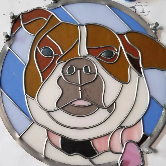 Stained glass artwork of a dog’s face featuring vivid colors and intricate metal outlines in a circular design.