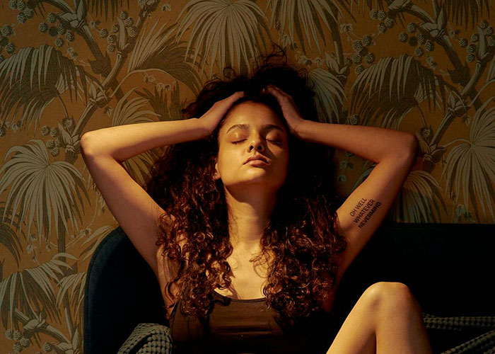 Woman with curly hair sitting relaxed with eyes closed, reflecting on insane things their ex did in wild stories.