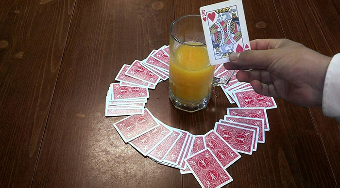 Hand holding King of Hearts card next to glass of orange juice surrounded by cards in a popular party game setup.