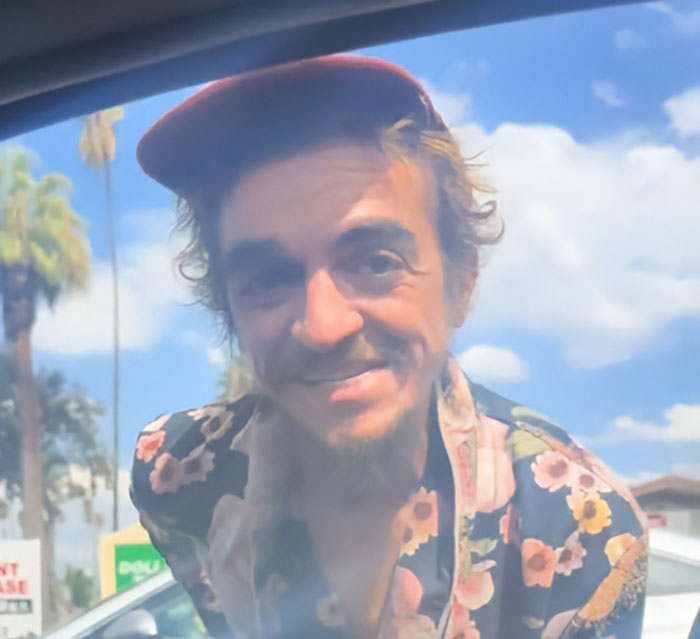 Nickelodeon star wearing a red cap and floral shirt, smiling outdoors in a video revealing homelessness struggle.