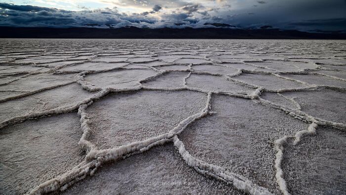 Salt flats with geometric patterns under a cloudy sky, showcasing one of the places that look AI generated but are real.