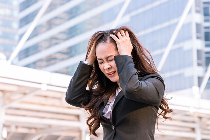 Frustrated woman in office attire holding her head, reacting to Christmas music blasting loudly at work. Frustrated woman in office attire holding her head, reacting to Christmas music blasting loudly at work.