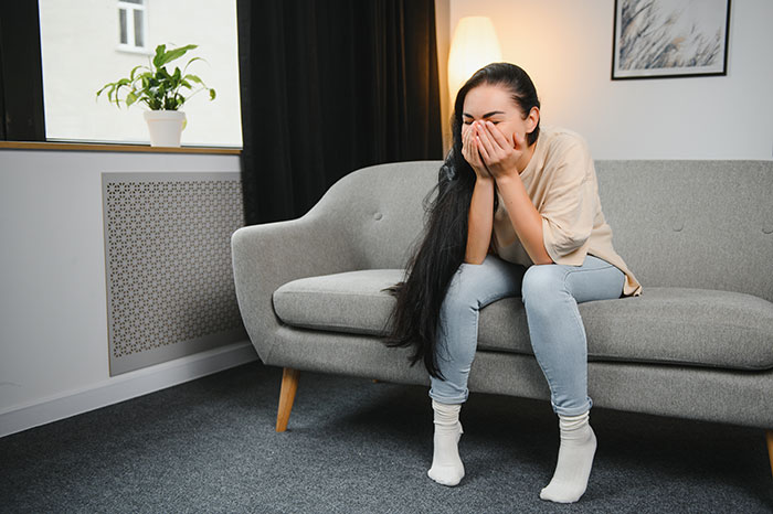 Young woman sitting on a couch, covering her face and crying, reflecting the pain of a wedding dress shopping friendship wake-up call. Young woman sitting on a couch, covering her face and crying, reflecting the pain of a wedding dress shopping friendship wake-up call.