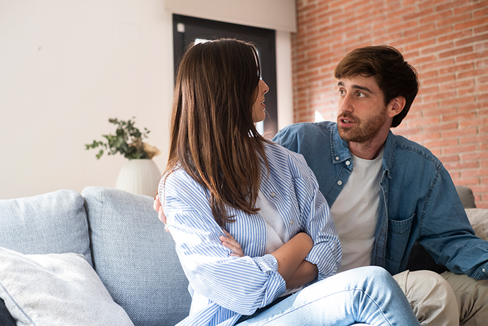 Couple having a tense conversation on sofa, highlighting boyfriend demanding girlfriend laser off all body hair.