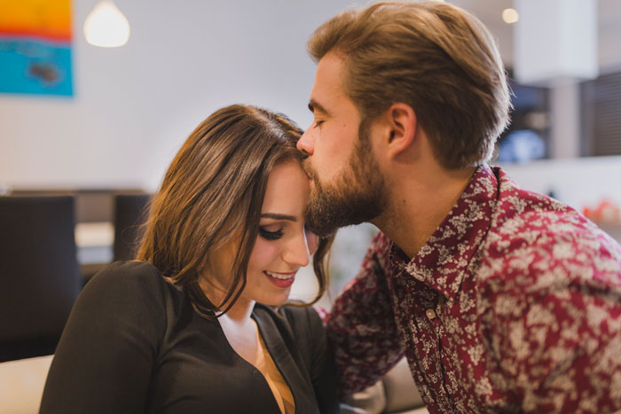 Pareja joven en oficina, hombre besa la frente de mujer, tema relacionado con escándalos en lugares de trabajo.