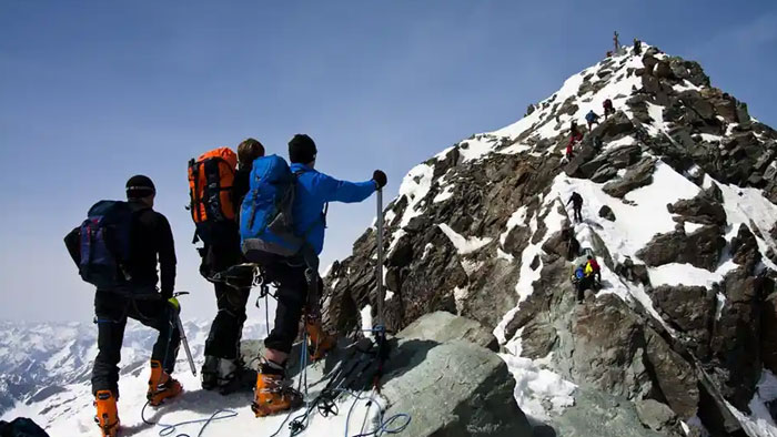 Three climbers in winter gear ascending Austria&rsquo;s highest peak with snow and rocky terrain under clear blue sky.