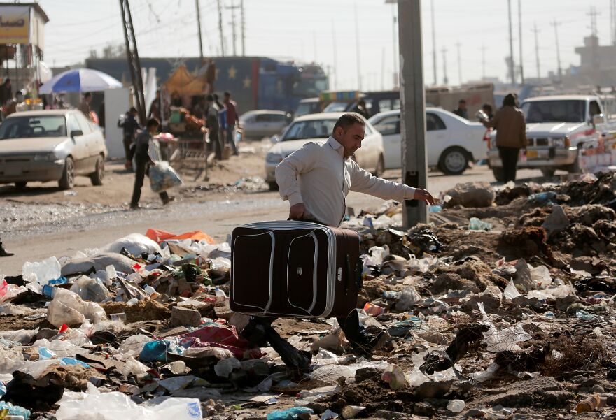 Man carrying suitcase walking through rubbish-strewn street in one of the dirtiest countries by pollution rankings.