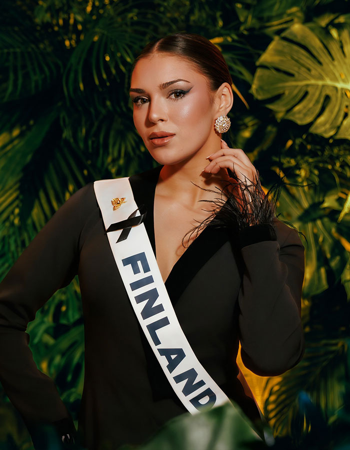Miss Finland wearing a sash posing confidently amid tropical leaves, linked to controversy and losing her crown.