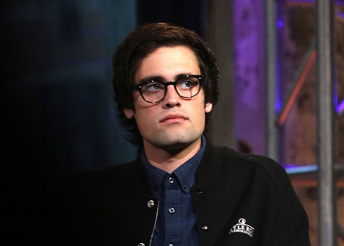 Young man wearing glasses and a dark jacket, looking thoughtful in a dimly lit setting related to Rob Reiner&rsquo;s son arrest news.