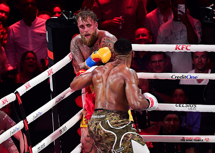Jake Paul defending in the boxing ring with bruised face as internet reacts to his broken jaw punchline.