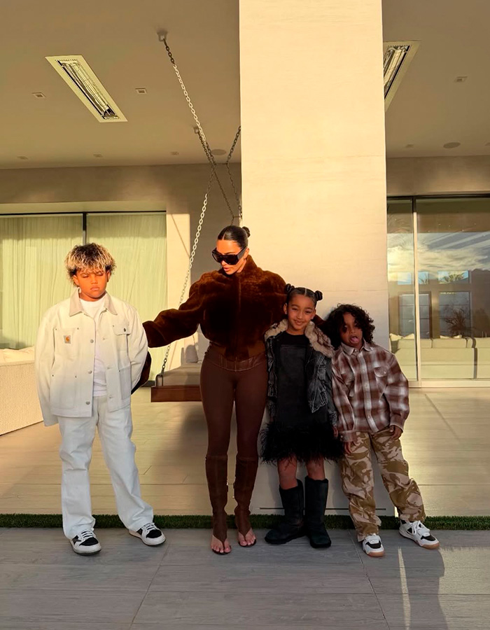 Kim Kardashian standing with her kids outside a modern home, reflecting fans' thoughts on kids' home life.