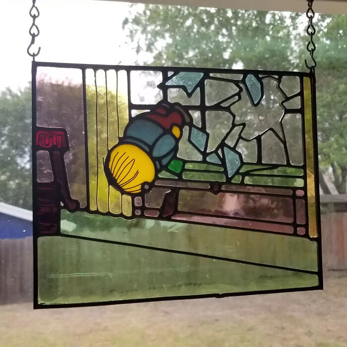 Stained glass sign depicting a pop culture icon in vivid colors, hanging against a window with trees outside.