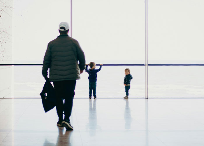 Man walking in an airport terminal near two children by large windows, illustrating airport seating and flight disputes.