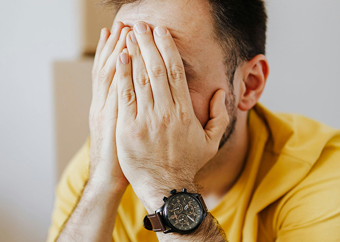 Man in yellow shirt covering face with hands, expressing frustration, related to 911 operators and non-emergency calls.