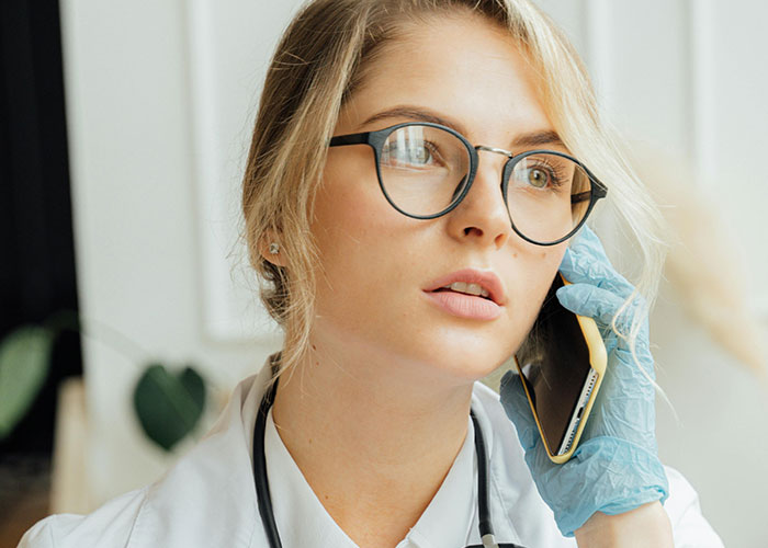 Female doctor wearing glasses and medical gloves speaking on phone, illustrating unprofessional things doctors have said to patients