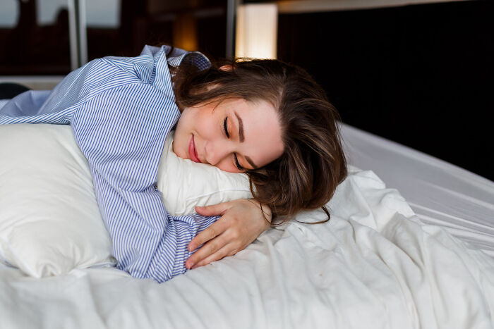 Young woman relaxing on a bed hugging a pillow, illustrating small tricks that make being a grown-up easier.