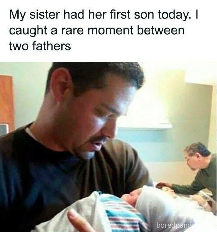 New dad holding his newborn son with another father looking on, capturing a sweet and wholesome moment.