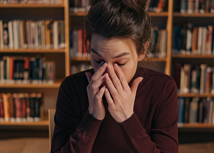 Woman in a maroon sweater rubbing her eyes, stressed in a library setting, reflecting tension with toxic mother-in-law during Christmas.