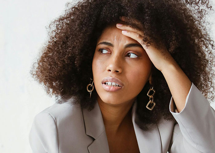 Woman with curly hair and anxious expression touching forehead, shocked by unhinged things her MIL said to her