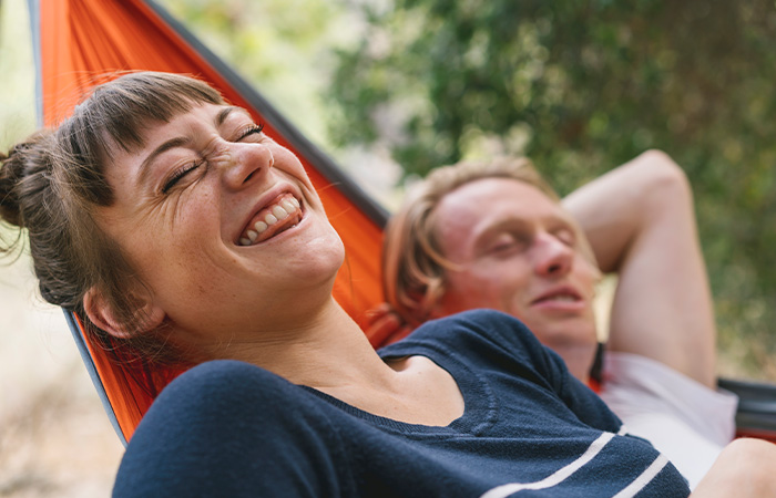 Smiling woman and relaxed man in a hammock outdoors, illustrating what men find attractive in women with genuine happiness.