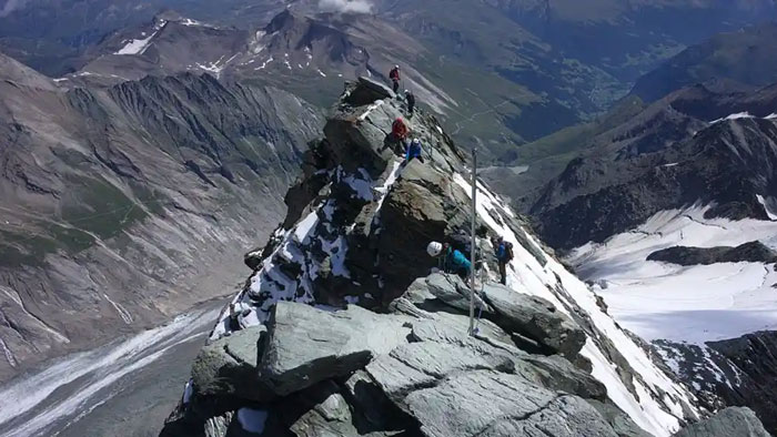 Climbers ascending Austria&rsquo;s highest peak with rocky terrain and snowy patches in a remote mountainous landscape.