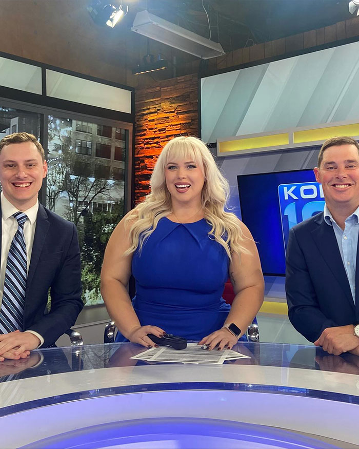 Curvy news anchor in blue dress sitting at news desk with two male co-anchors during a broadcast segment. Curvy news anchor in blue dress sitting at news desk with two male co-anchors during a broadcast segment.