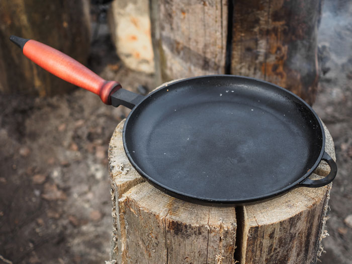 Cast iron pan with wooden handle placed on a tree stump, a white elephant gift perfect for stealing at parties.