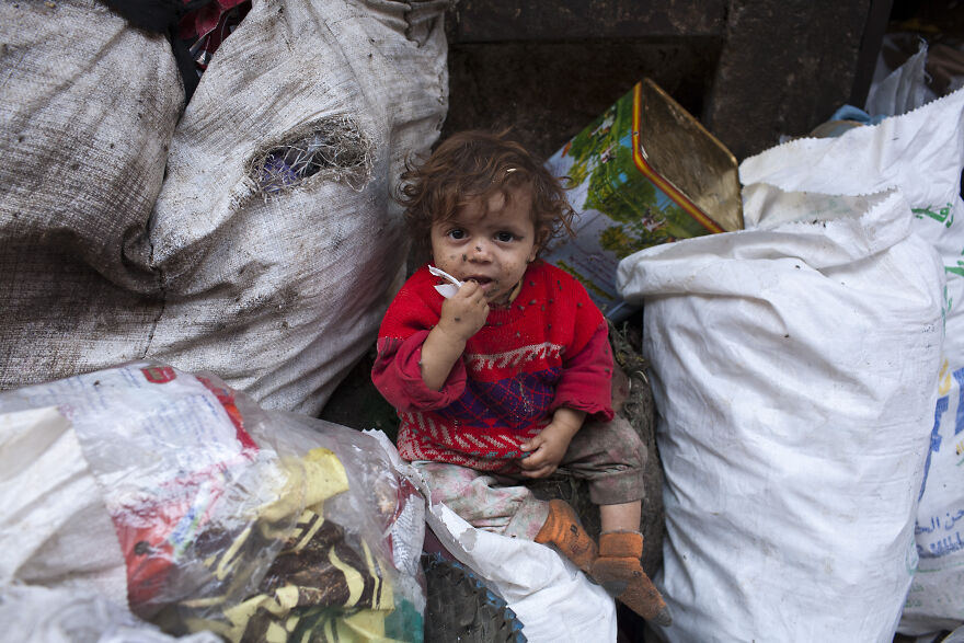 A young child sitting amid large trash bags and debris, highlighting pollution in the dirtiest countries in the world.