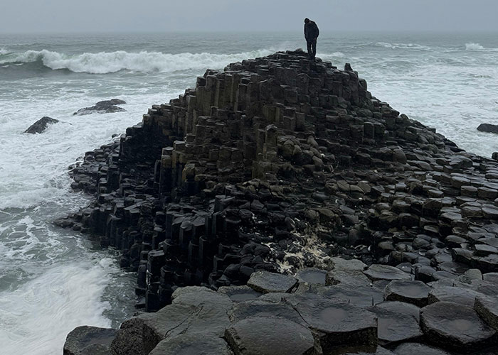 Person standing on hexagonal basalt columns by the ocean, a natural place that looks AI generated but is real.
