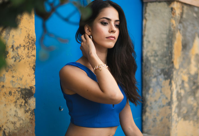 Young woman in a blue crop top posing thoughtfully against a textured wall, reflecting on things men can’t stand.