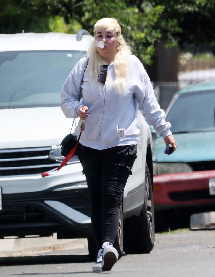 Amanda Bynes walking outdoors, wearing a gray hoodie and black pants, amid paparazzi photos showing dramatic weight loss and injections.