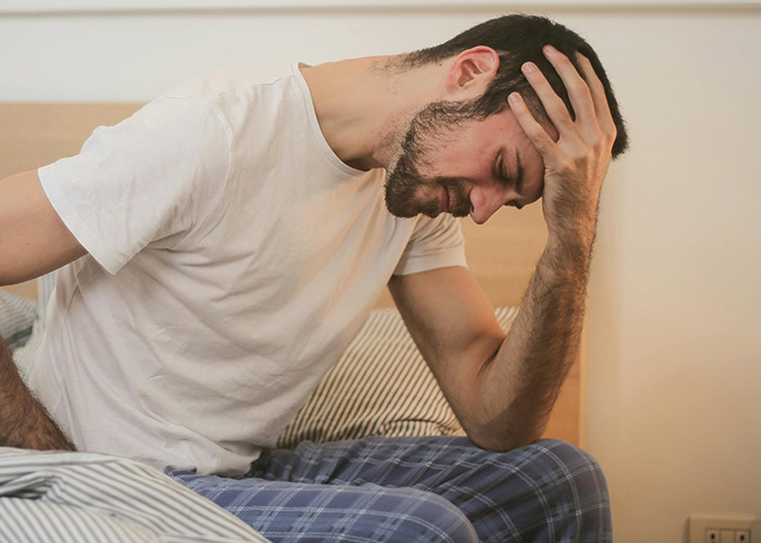 Man in pajamas sitting on bed holding head in frustration, illustrating dumbest non-emergency 911 calls concept